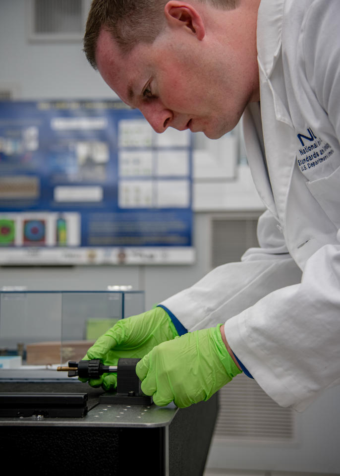 Man in lab coat leans over bullet in holder.
